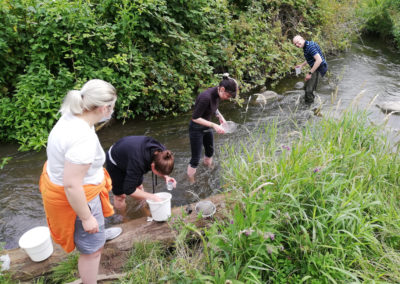 Schüler stehen in einem Bach und nehmen Wasserproben